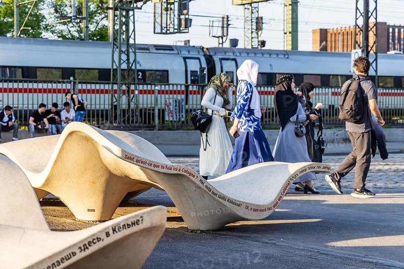 New seating on Norbert-Burger-Platz at the end of the Hohenzollern Bridge on the right bank of the Rhine. Inscription in various languages: What do you want in Cologne? Group of woman with headscarves. Cologne, North Rhine-Westphalia, Germany