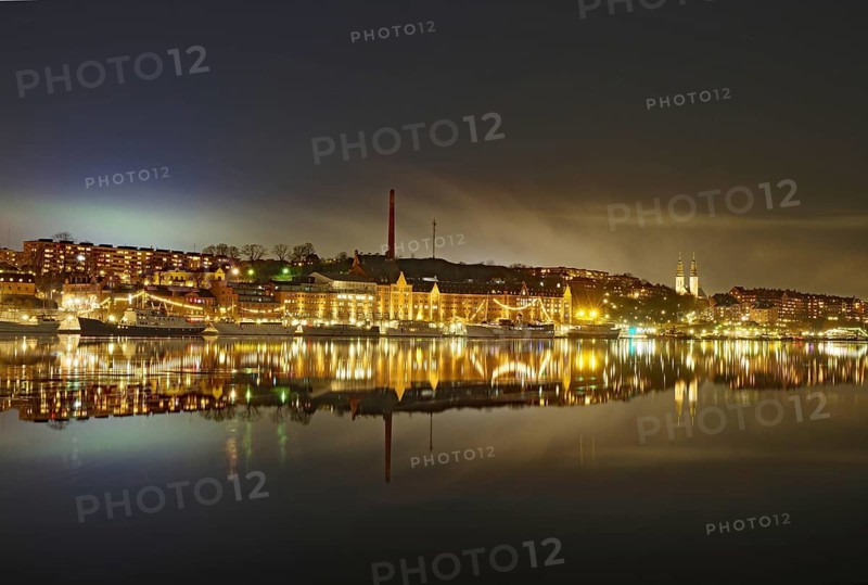 Illuminated buildings reflected in calm water, surrounded by light haze at night, faint aurora borealis, capital city, Södermalm, Stockholm, Sweden