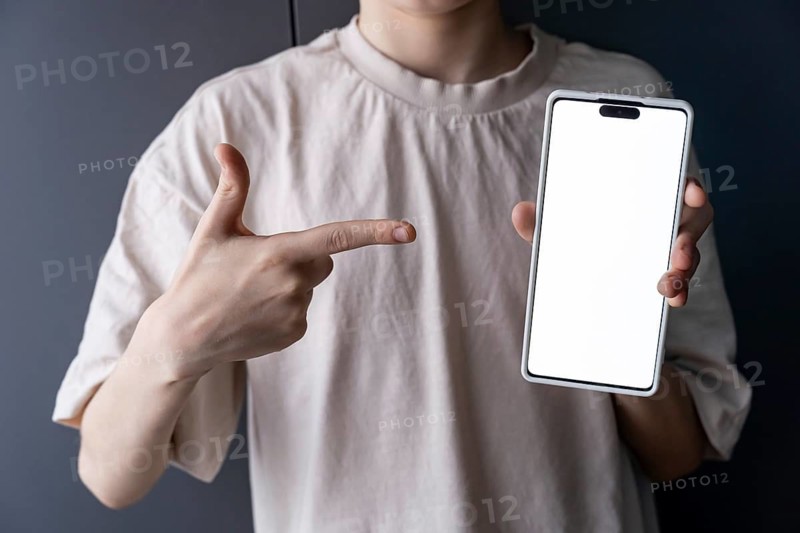 Teenage boy points at a smartphone with a blank screen, ideal for showcasing gaming apps. The image can be used for technology, gaming, and app promotions