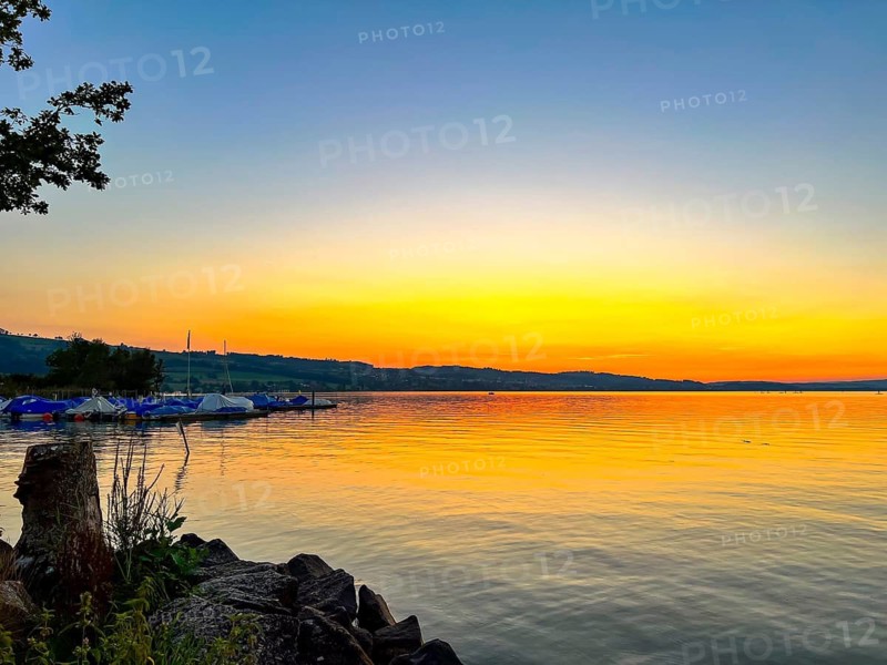 Lake Sempach at sunset with a bright, colourful sky and boats on the shore, Sempach, Lucerne, Switzerland