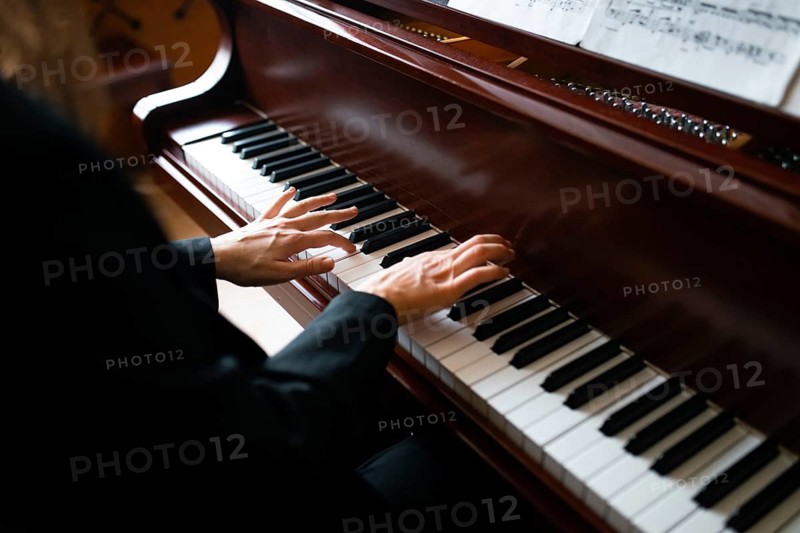 A skilled musician plays a grand piano, fingers gracefully dancing on the keys, while sheet music rests on the stand, creating an atmosphere of classical elegance and passion