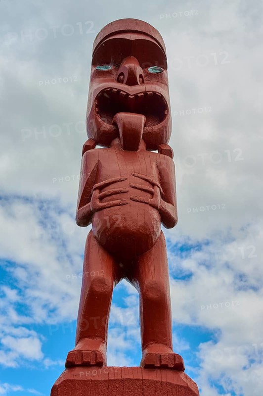 Red wooden figure of maori art with expressive face and hands on stomach, New Zealand Maori Arts and Crafts Institute, Te Puia, Whakarewarewa, Rotorua, North Island, New Zealand