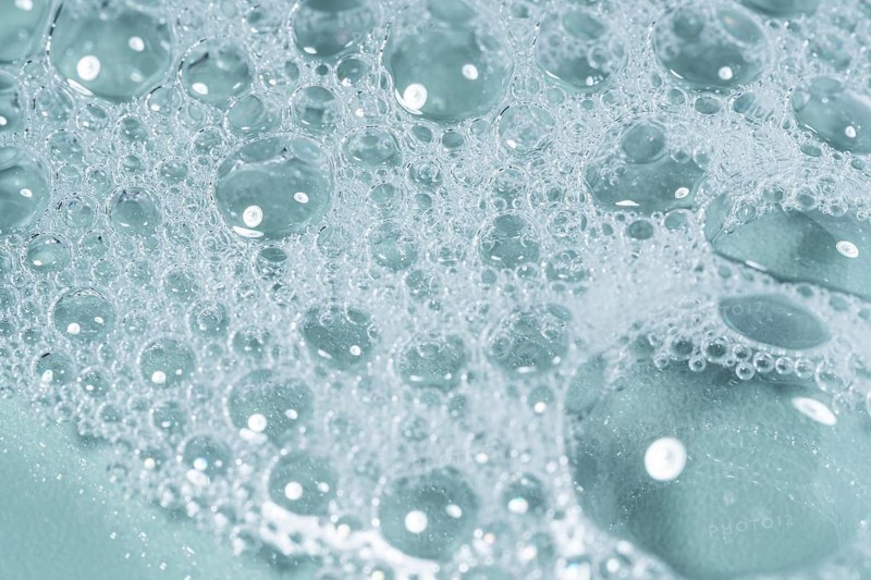 Top view of transparent gel bubbles forming intricate patterns on a laboratory glass surface. The delicate bubbles create a mesmerizing texture against a subtle blue background
