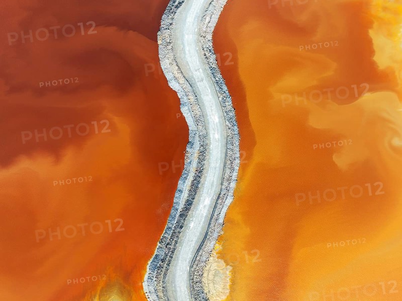 Track crossing a waste pond in the mineral-rich area of the Rio Tinto mines. The colour is caused by oxidised iron minerals. Aerial view. Drone shot. Huelva province, Andalusia, Spain