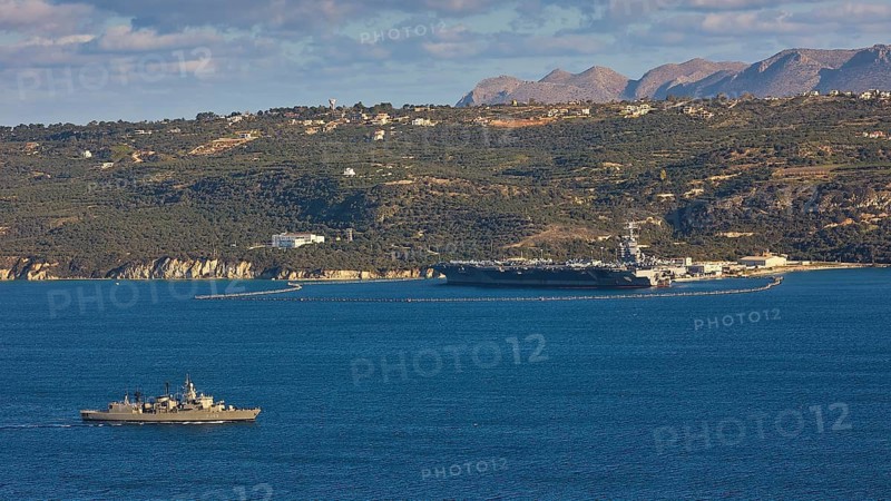 Aircraft carrier USS Gerald R. Ford, largest aircraft carrier in the world, anchored in Souda Bay on February 24, 2026, Greek Navy S-class frigate Kountouriotis, military ship on blue sea off a wooded coast, US Navy, Souda Bay, Akrotiri Peninsula, Chania Province, Crete, Greek Islands, Greece