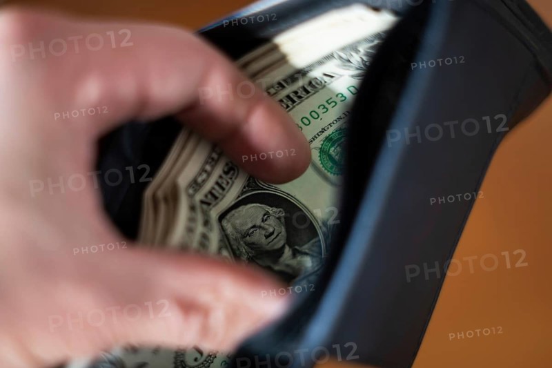 A blurred hand places or taking folded US dollar bills, with George Washington's portrait visible, into a dark wallet. Concepts of savings, payment, budget, and finance in Poland