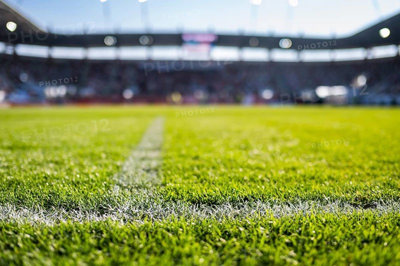 Close-up low-angle view of a white chalk boundary line on a vibrant green soccer pitch with a blurred stadium in the background in Lubin, Poland