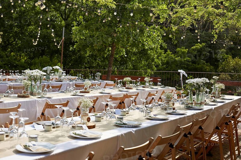 Beautiful boho wedding table setup outdoors featuring white floral arrangements in glass vases. Wooden chairs and tables with elegant tableware create a romantic atmosphere