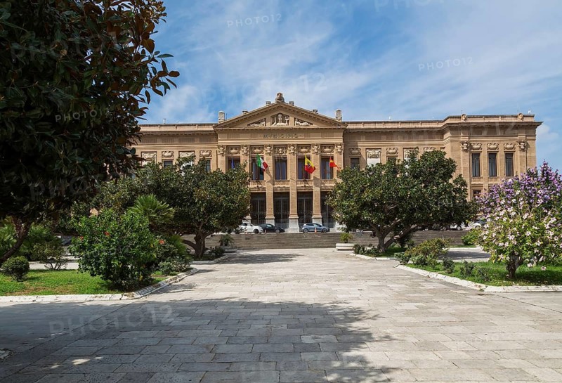 Neoclassical style Zanca Palace or the Messina Town Hall building facade through landscaped park with Nerium - Oleander shrub and Hibiscus trees in late summer, Messina, Sicily, Italy