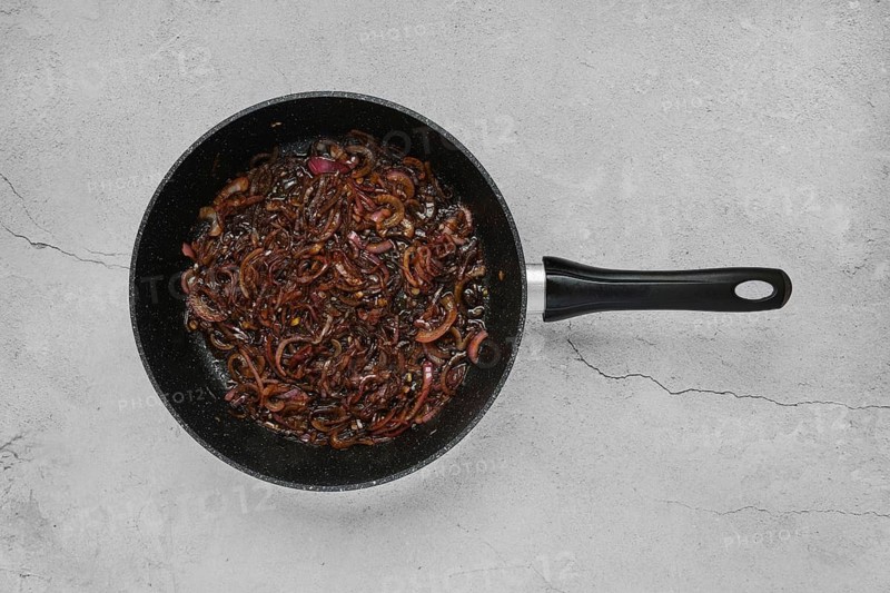 Caramelised onions are being sautéed in a black frying pan, turning rich brown while releasing their sweet aroma