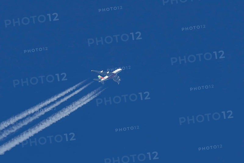 Airbus A380 jet passenger aircraft of Emirates airlines flying in a blue sky with contrails or vapour trails behind, England, United Kingdom