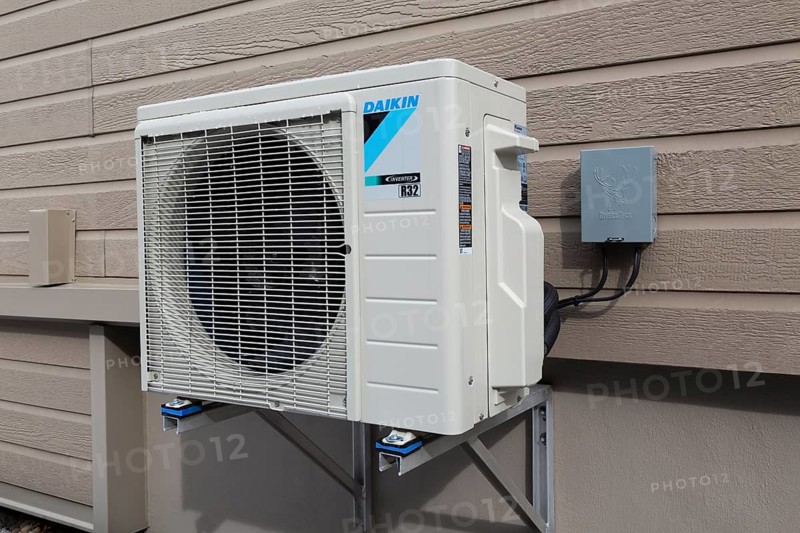 Daiken Inverter R32 air conditioning heat pump (condenser unit) and electrical disconnect box (external safety switch) mounted on outside wall of home, Quebec, Canada