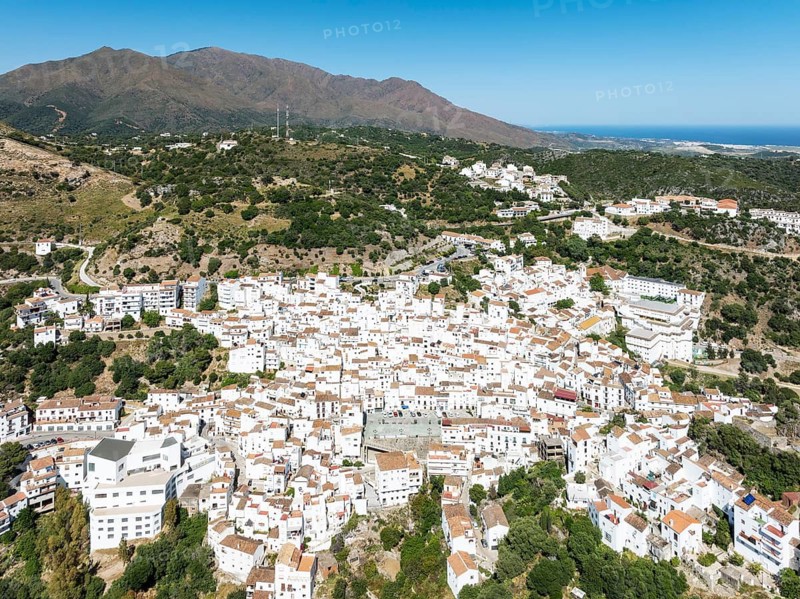 The brilliant White Town of Casares clings to a steep hillside. In the background the Sierra Bermeja and the Mediterranean Sea. Aerial view. Drone shot. Málaga province, Andalusia, Spain