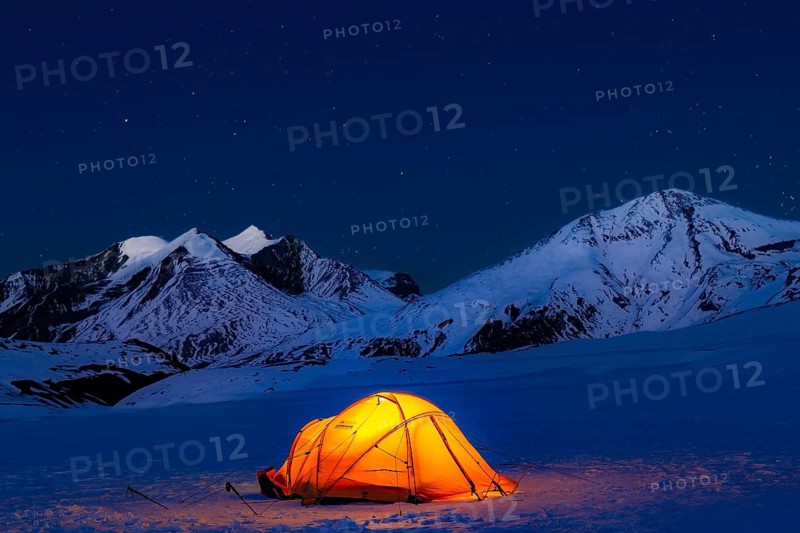 Illuminated tent in snow against snow-covered mountains and starry sky in Hidden Valley, plateau at 5100 m between French Pass and Dhampus Pass, Dhaulagiri Trekking, Dhaulagiri Himal, Himalayas, Nepal