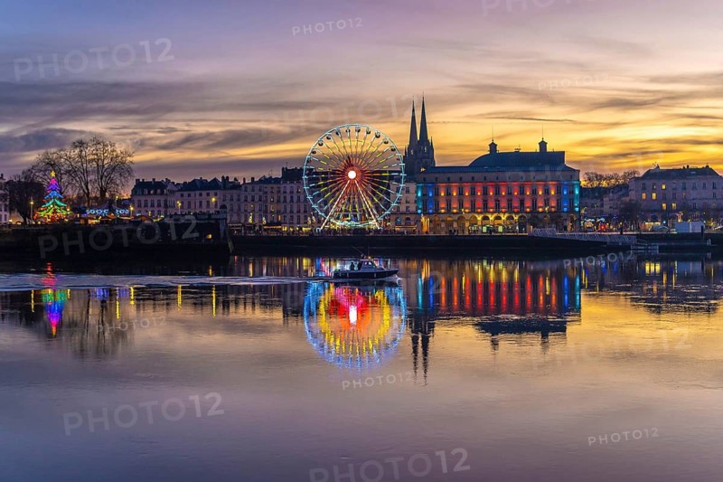 Bayonne cityscape illuminating the adour river with colorful christmas lights, a ferris wheel, and a decorated tree creating a festive evening reflection under the twilight sky