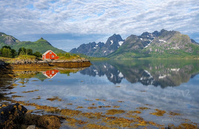 Red fishing hut on the shore, Rorbuer hut, picturesque fjord landscape at Raftsund fjord, mountains reflected in water, Vesterålen, Norway