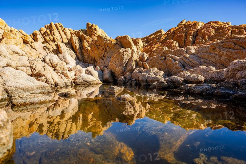 Reflection of stones in a puddle of water from the rocks on the beach at Marinedda Coast on a sunny day, Sardinia, Italy