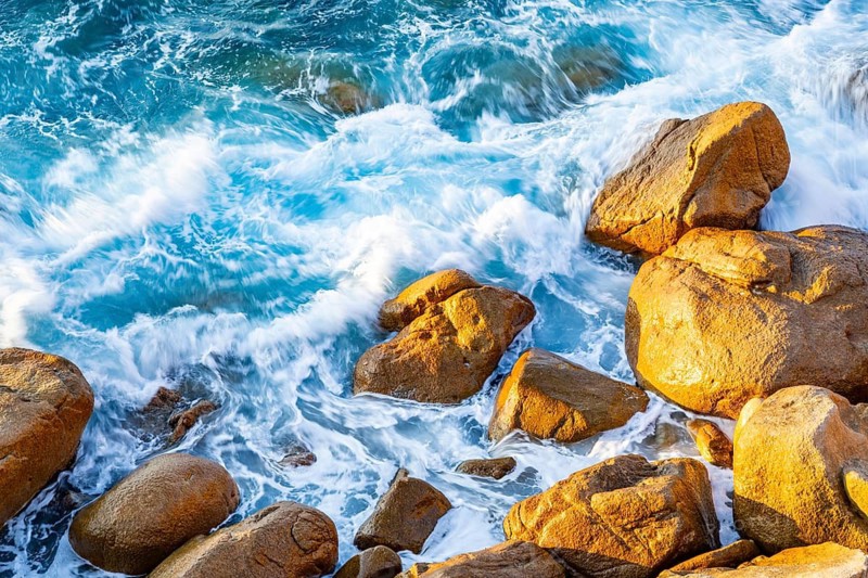 Surf at the coastline, blue water flows around the stones at Costa Paradiso in eveneing light, Sardinia, Italy