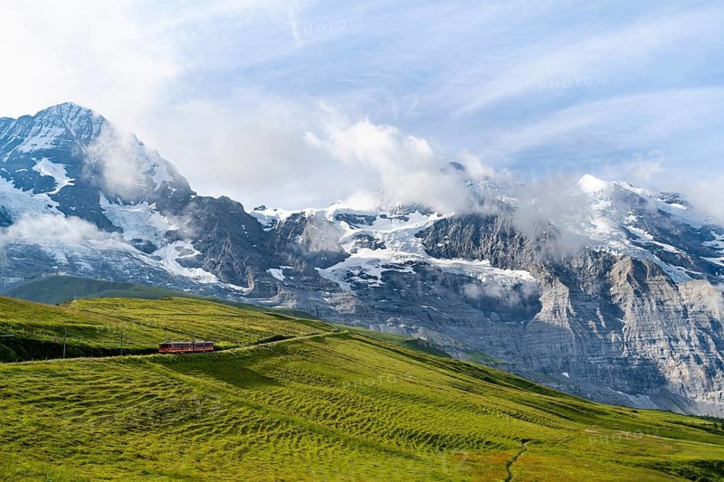 Jungfrau Railway to Jungfraujoch runs through green meadows, above the Kleine Scheidegg stop, rack railway, in the back mountains with peaks Eiger, Mönch and Jungfrau, Jungfrau region, Bernese Oberland, Switzerland
