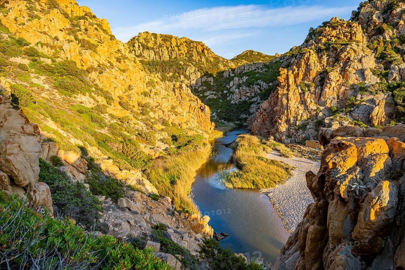 A small river flowing through the mountains into the sea, past a sandy beach in Costa Paradiso on a sunny evening, Sardinia, Italy