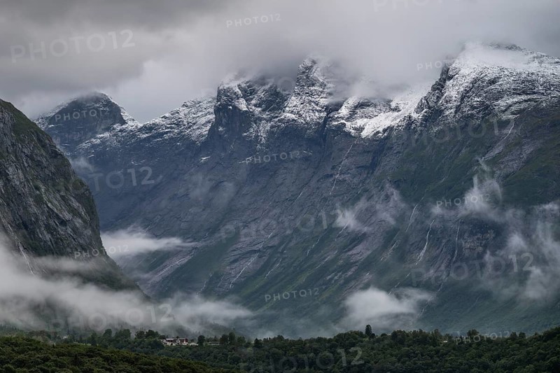 Freshly snow-covered mountain range above a valley and low-hanging scraps of clouds on the valley slopes, near Åndalsnes or Andalsnes, Rauma municipality in the province of Møre og Romsdal, Norway