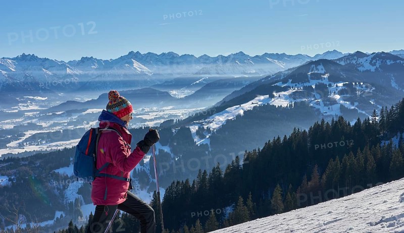Nice and active senior woman snowshoeing in in the snow covered Allgaue alps above the valley of river Iller, Immenstadt, Bavaria, Germany