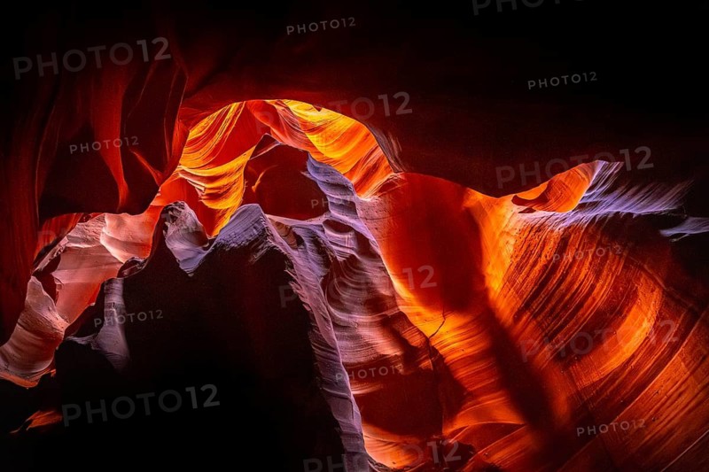 Slot canyon walls showing sunlit sandstone formations with vibrant orange, red, and purple hues creating a natural abstract underground landscape in arizona