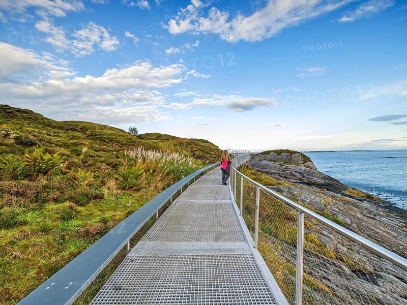 Person on a coastal promenade with a view of the sea and a cloudy sky, circular route along the Atlantic road, blue sky with clouds, sunrise, Atlanterhavsveien, Møre og Romsdal, Norway