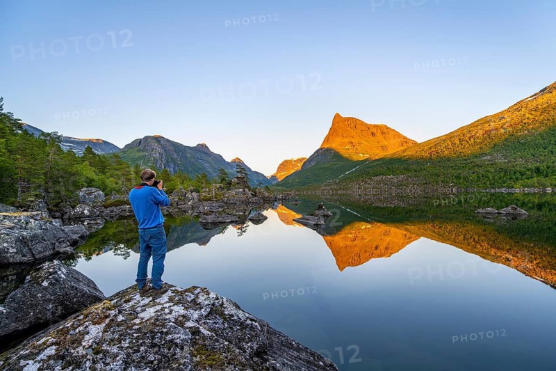 Young man photographed, picturesque mountain landscape in the Innerdalen high valley with Innerdalstårnet summit, mountain peaks reflected in lake Innerdalsvatna, in the evening light at sunset, Trollheimen Mountain Area, Sunndal, Møre og Romsdal, Norway