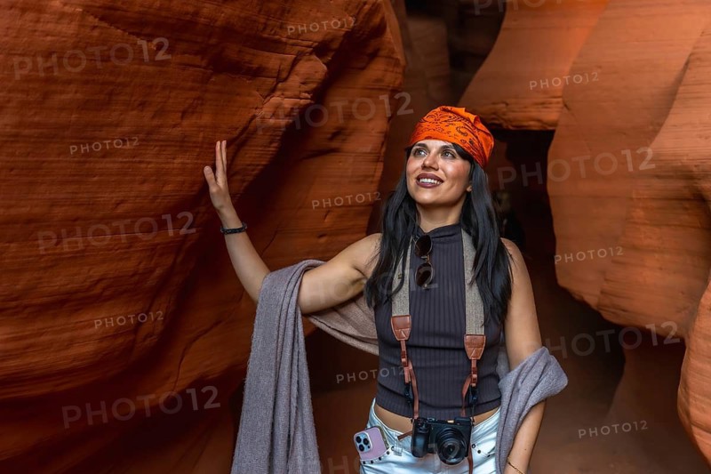 Woman standing inside antelope canyon, touching the textured sandstone wall while gazing upwards, captivated by the light and the natural rock formations during a solo travel adventure