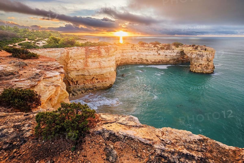 Golden sunrise over the ocean at Praia de Albandeira beach in Algarve, Portugal, with Arco de Albandeira and rugged cliffs