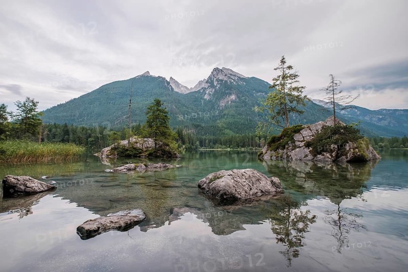 Wide angle view of the transparent water at Hintersee lake featuring rocky islands and the Hoher Goll mountain range in Germany