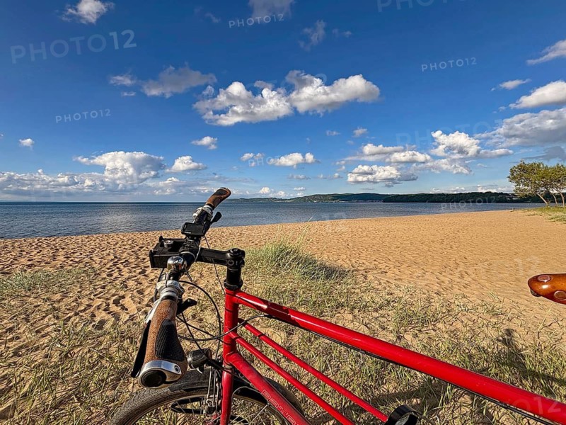 Red bicycle on sunny sandy beach under blue sky with clouds and sea in the background, Lake Vättern, Jönköping, Sweden
