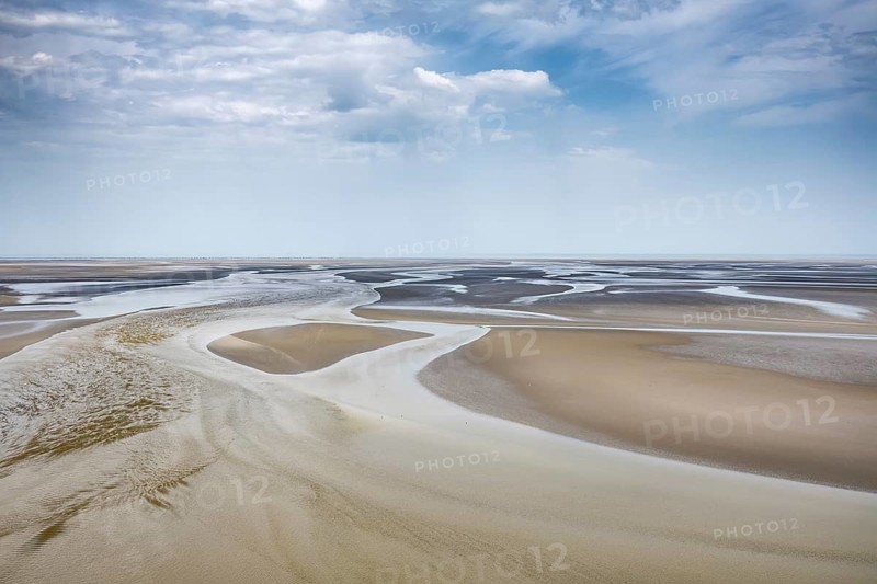 View from the rocky island, monastery island of Le Mont Saint Michel onto a wide mudflat landscape with creeks and dramatic clouds at low tide, Mont-Saint-Michel Bay, Pontorson, Manche department, Normandy, France