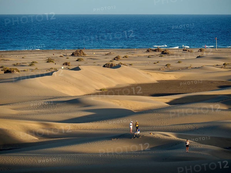 People walk across dunes on the beach in the light of the evening sun, Maspalomas Dunes, Gran Canaria, Spain