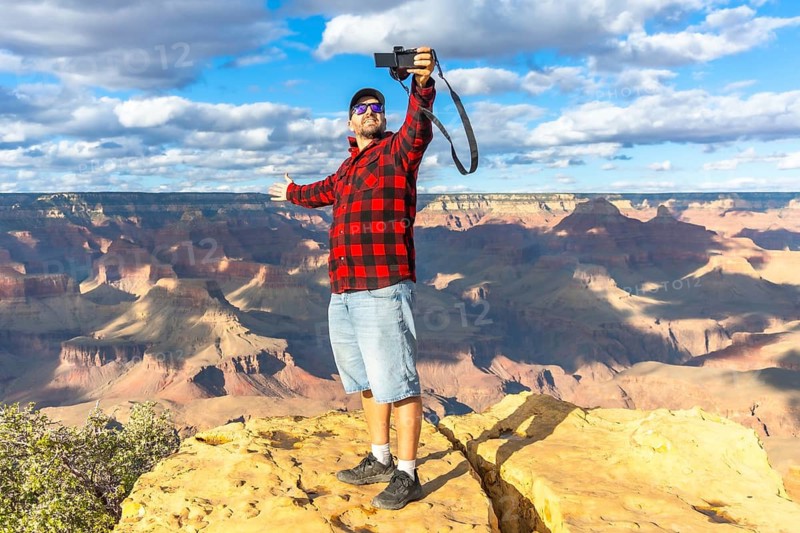 Man standing with arms outstretched on a rocky cliff, capturing a video selfie with his phone, experiencing freedom and happiness during a travel adventure at the vast grand canyon national park