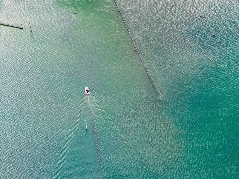 Motorboat entering the port of moss. Waves form on the surface of the water. The water level in Lake Constance is at a low level due to the hot summer. In many ports in the Untersee, there is barely any water left. moss is located on the shores of Lake Constance on the Höri peninsula. aerial view. moss, Baden-Württemberg, Germany