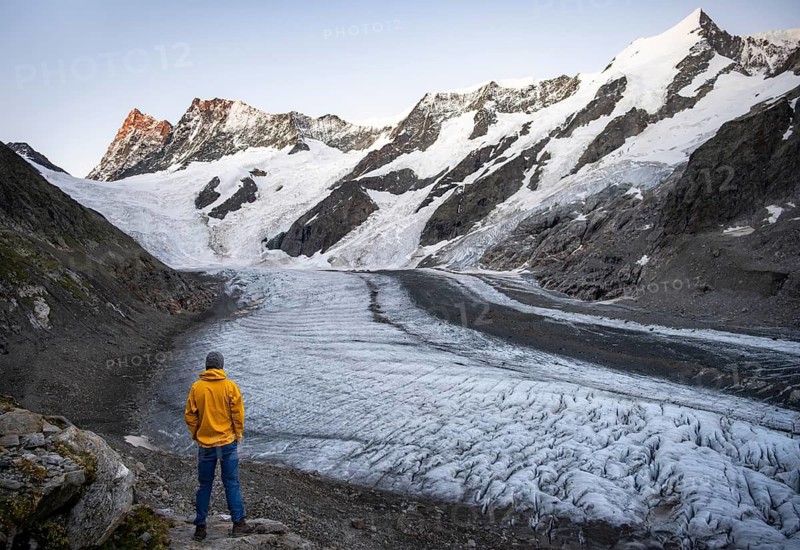 Young man in front of impressive high-alpine landscape, Finsteraarhorn and Agassizhorn mountain peaks with alpine glow at sunrise, Upper Arctic Ocean glacier, Bernese Alps, Bernese Oberland, Switzerland