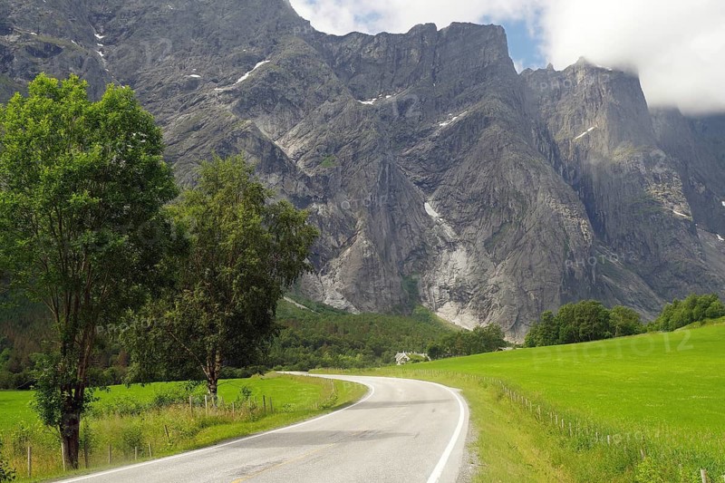 Winding country road between green fields and dramatic mountains under cloudy sky, Tom Cruise filming location, Raumadalen, Trollvegen, Andalsnes, Norway