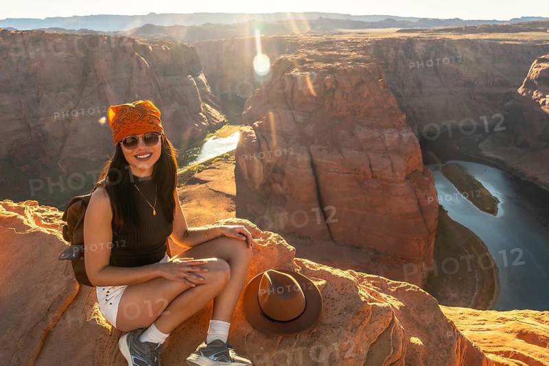 Young woman smiling while sitting on a cliff edge, overlooking the colorado river winding through the grand canyon landscape at sunset in page, arizona