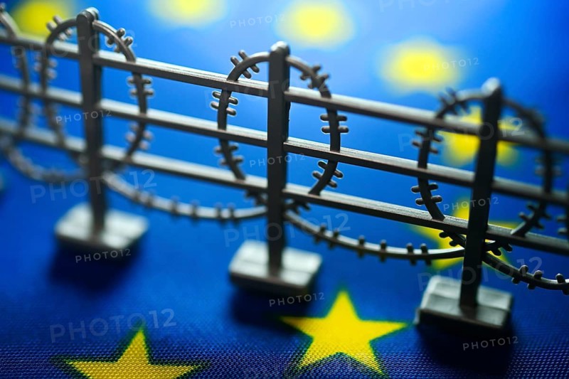Miniature fence with barbed wire on EU flag, symbolic photo of European asylum reform +++ editorial use only