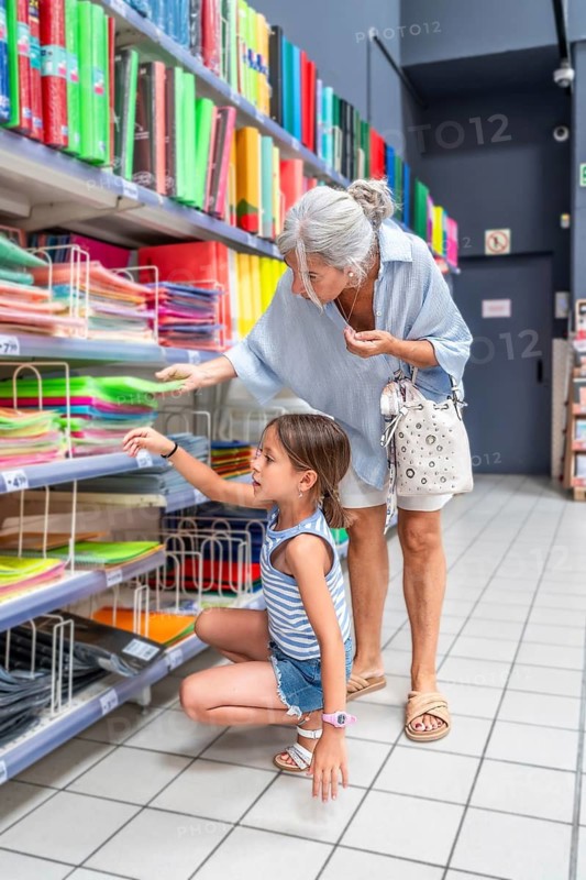 Grandmother and granddaughter choosing colorful folders and binders from a retail store shelf, preparing for school and enjoying a bonding experience during their shopping trip