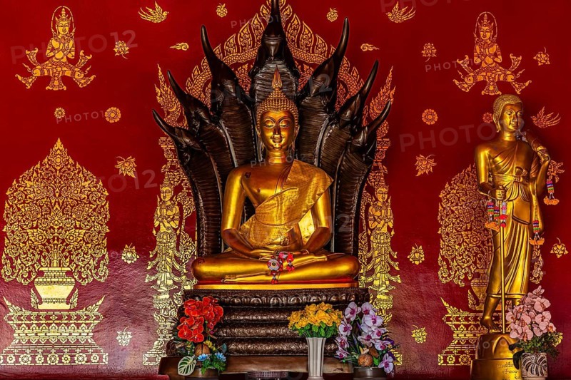 Gilded seated Buddha statue in front of artfully decorated red temple wall, Buddhist temple complex Wat Phra That Si Chom Thong, near Chiang Mai, Chiang Mai Province, Thailand