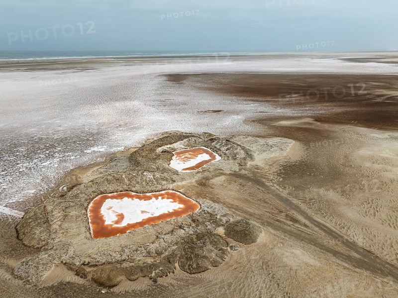 Saline ponds with ruddy algae growth and white salt deposits at the Atlantic Coast. Aerial view. Drone shot. Namib Desert, Skeleton Coast, Dorob National Park, Namibia