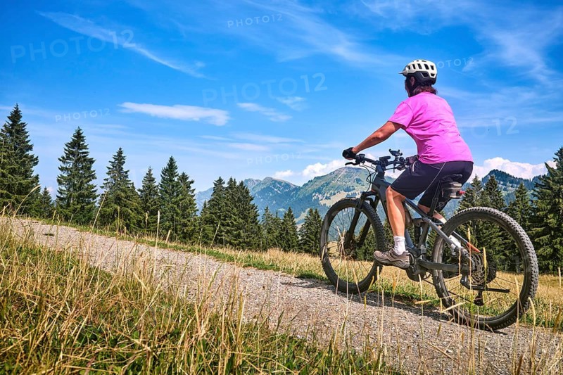Active senior woman rides an e-mountain bike on a picturesque mountain trail under the Nagelfluh Mountains, Oberstaufen, Allgäu, Bavaria, Germany