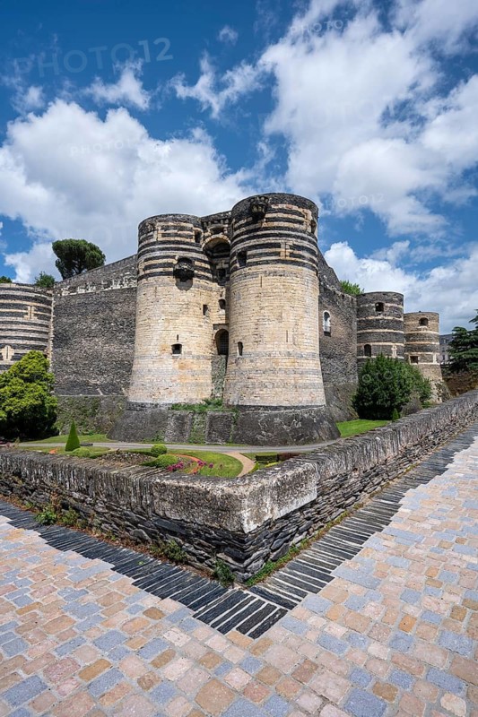 Monumental castle complex from the 13th century with distinctive tower architecture, nestled in a well-kept park and garden landscape with symmetrical patterns in the deep ditch in front of the fortress walls, Château d'Angers, Angers, Maine-et-Loire, Pays de la Loire, France