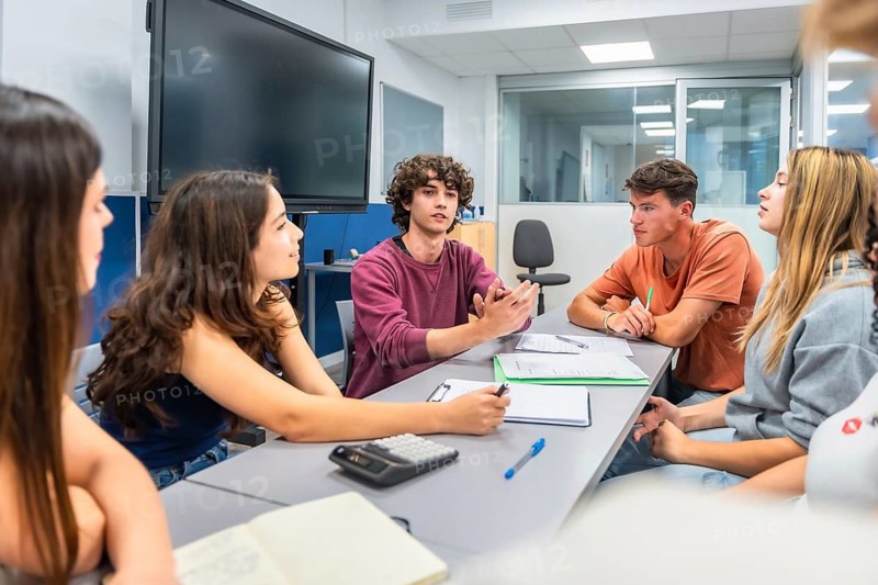 Young students actively participate in a collaborative study group, discussing project ideas and sharing insights at a meeting table in a modern university classroom environment