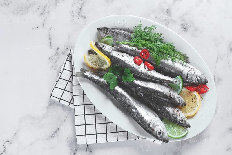 Fresh Herring fish, ready to cook, with herbs and spices, on a white platter, in the kitchen