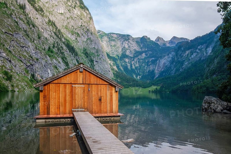 Iconic wooden boathouse on the shore of Obersee lake with a stunning backdrop of the high Alps in Bavaria, Germany near Konigssee