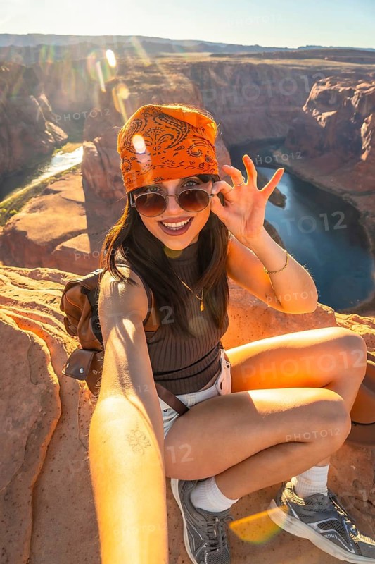 Woman traveler enjoying a scenic adventure at horseshoe bend overlook, capturing a cheerful selfie at sunset with the colorado river meandering through the canyon landscape